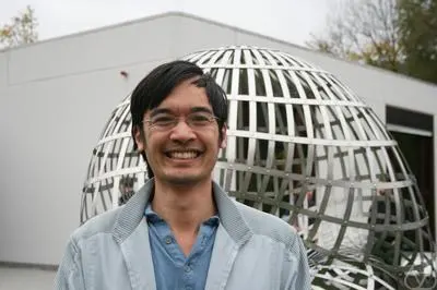 Terence Tao smiling outdoors in front of a large metal sphere sculpture.