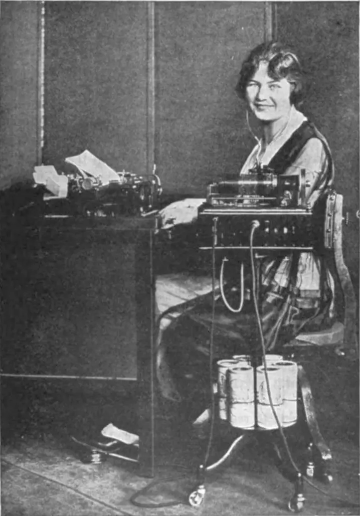 A woman in the early 1920s wearing headphones and typing up dictation recorded on a wax cylinder Dictaphone